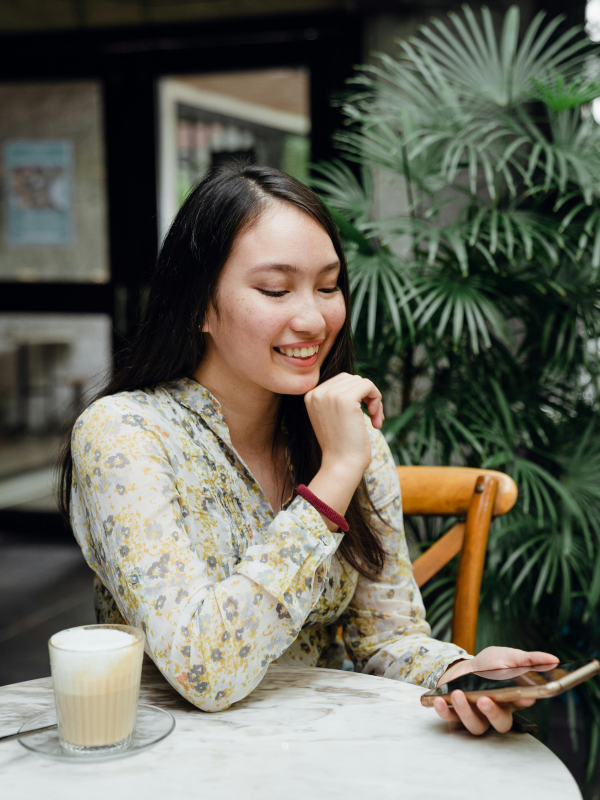 Woman sitting with coffee and leaving online review on mobile phone.