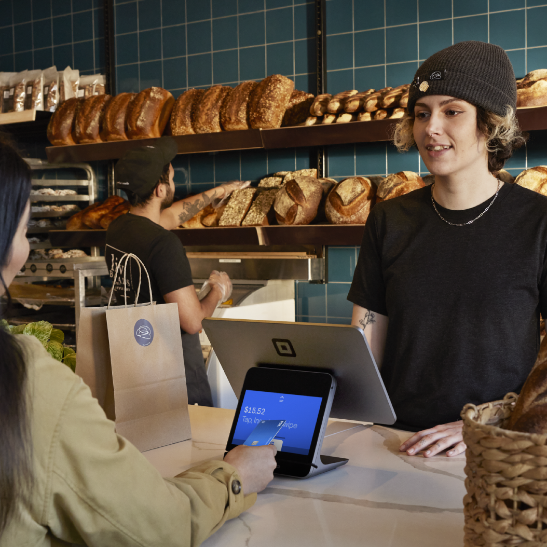 Female customer inside bakery tapping credit card on Square POS operated by female cashier.