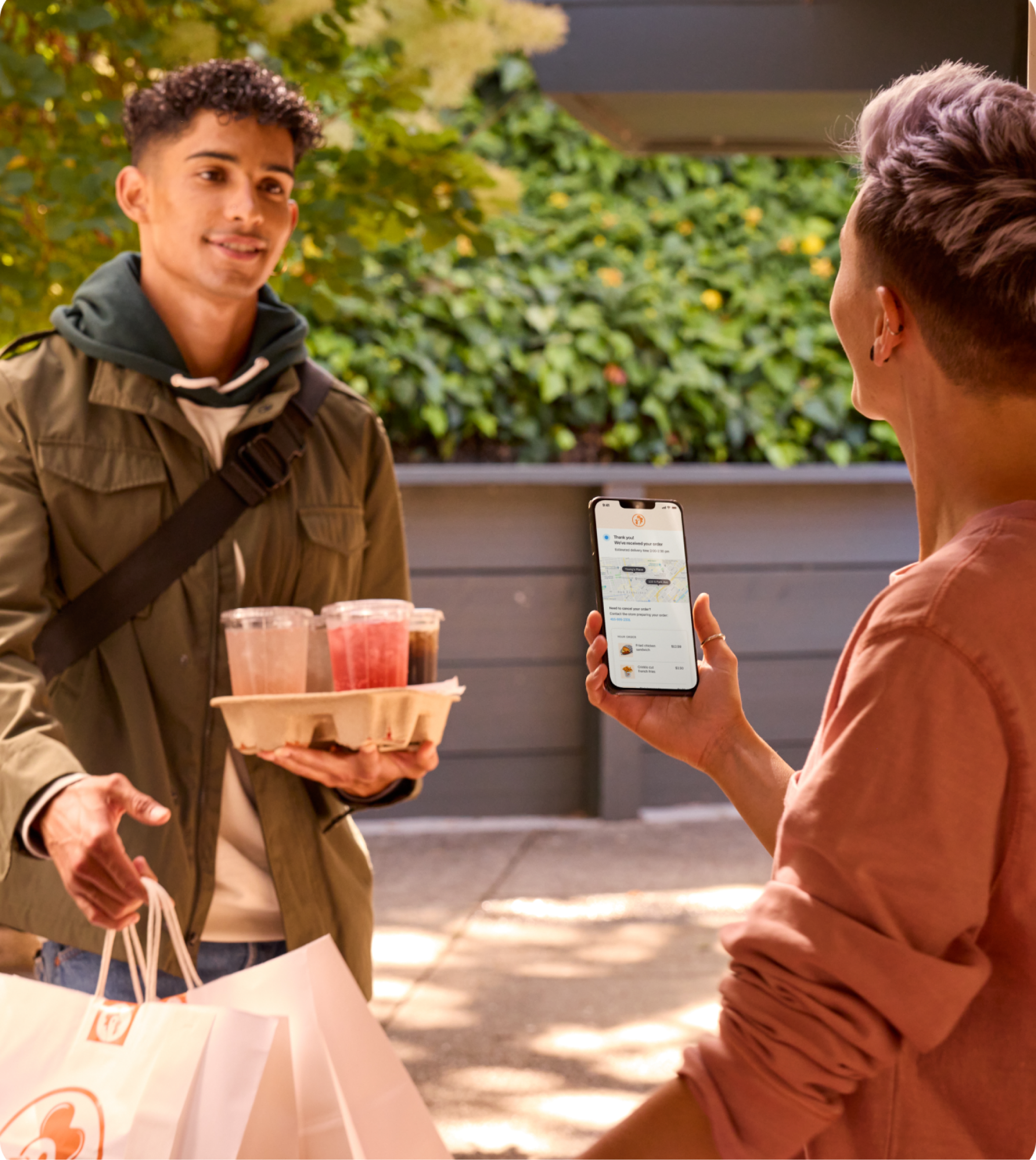 Male restaurant employee deliverying food to customer holding phone displaying Square mobile app.