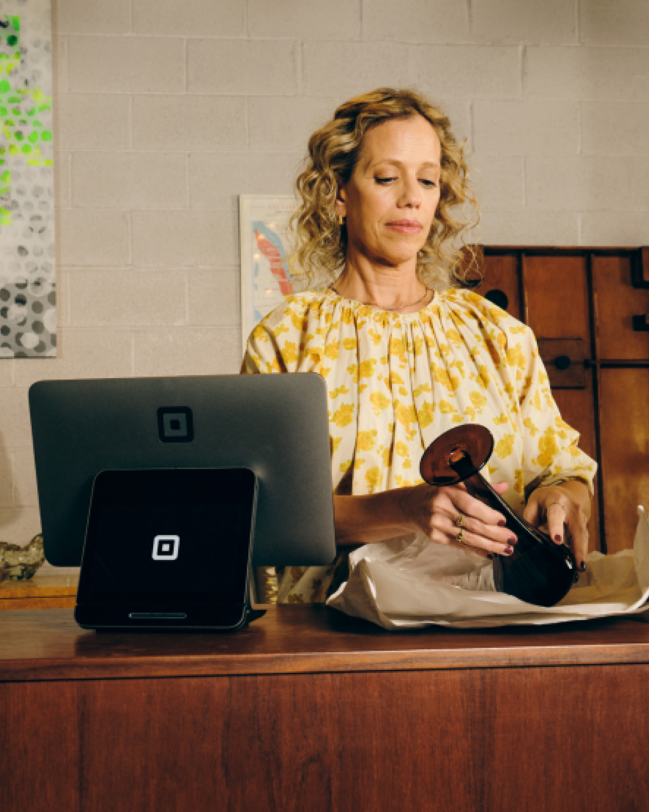 Female cashier wrapping product near Square register.