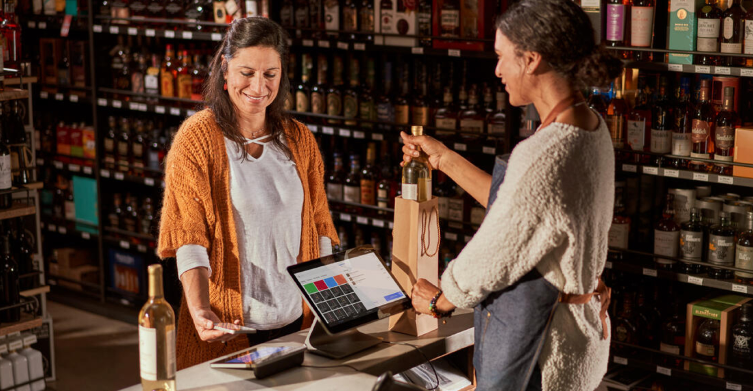 Wine shop female cashier checking out female guest at Square register.